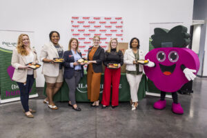 Six representatives of the Summer LunchBox Program stand in a row and hold meals in front of them with the philabundance mascot 